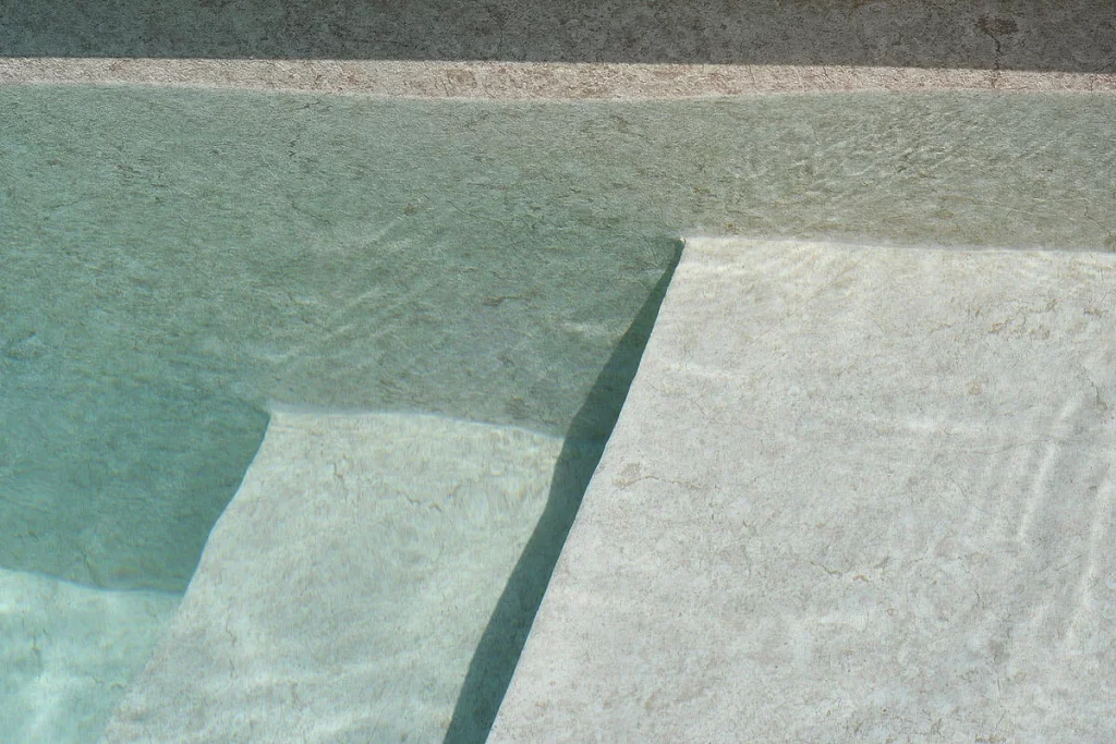Membrana armada Sublime en agua, reflejando la claridad y la profundidad característica del mármol travertino en su máxima expresión, creando un ambiente de serenidad.