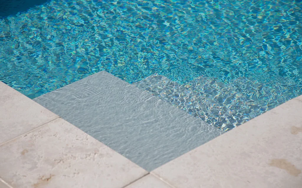 Detalle de esquina de piscina minimalista con membrana armada gris claro, perfecta para relax.